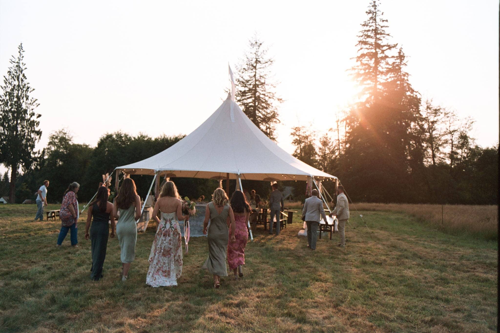Guests migrate to an outdoor wedding reception under at tent. Photo shot on film.