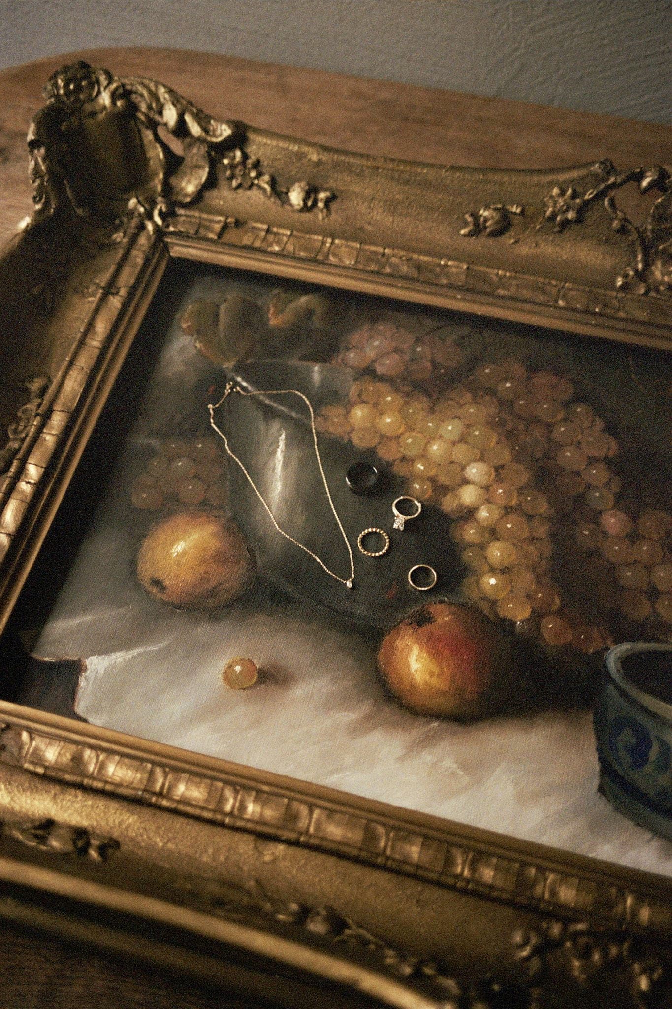 Wedding jewelry resting on an Italian painting of fruit.