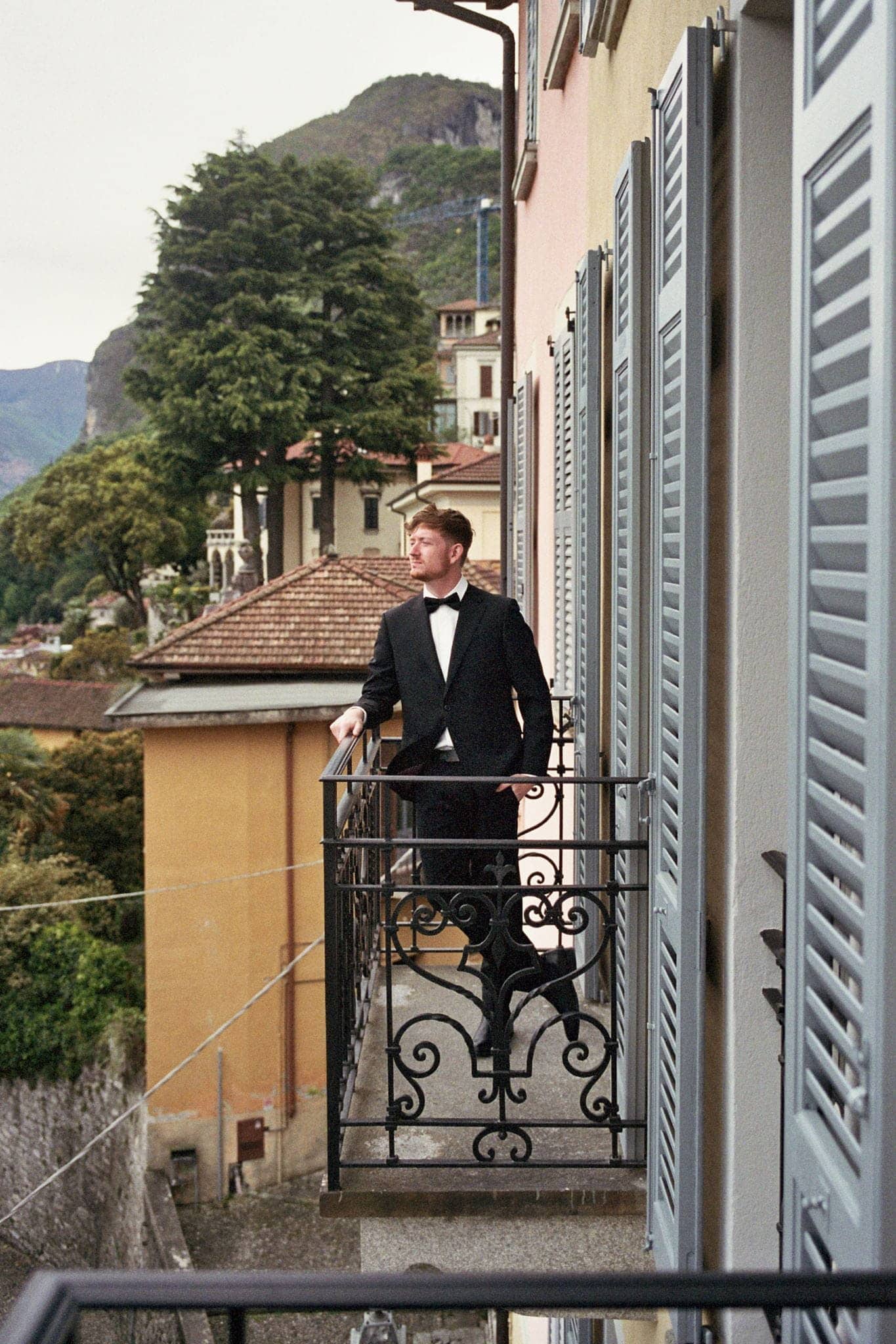 Film wedding photo of groom leaning against a patio railing in his Italian villa while waiting for his wedding first look.