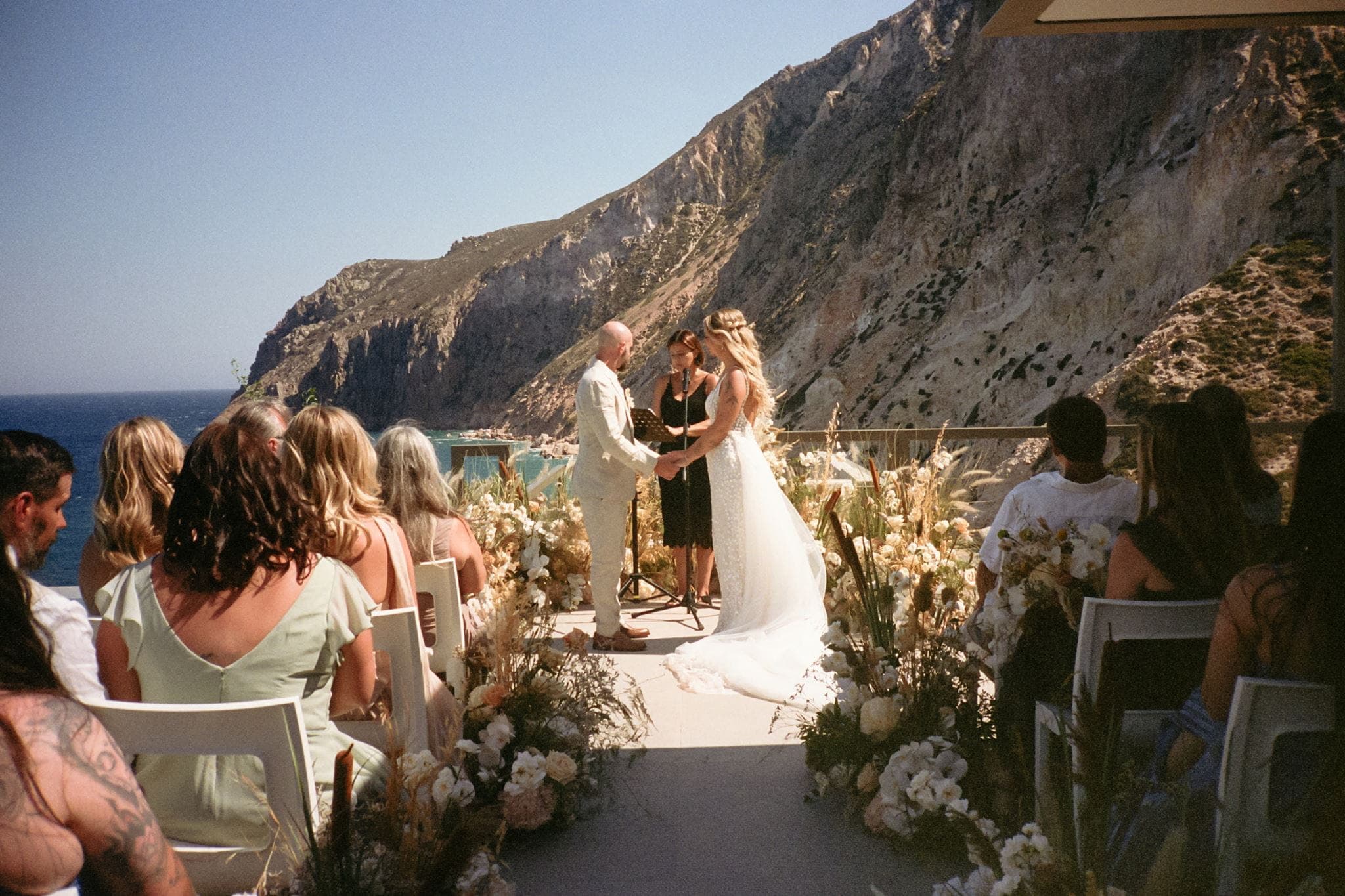 Bride and groom hold hands during their film wedding ceremony in Greece.