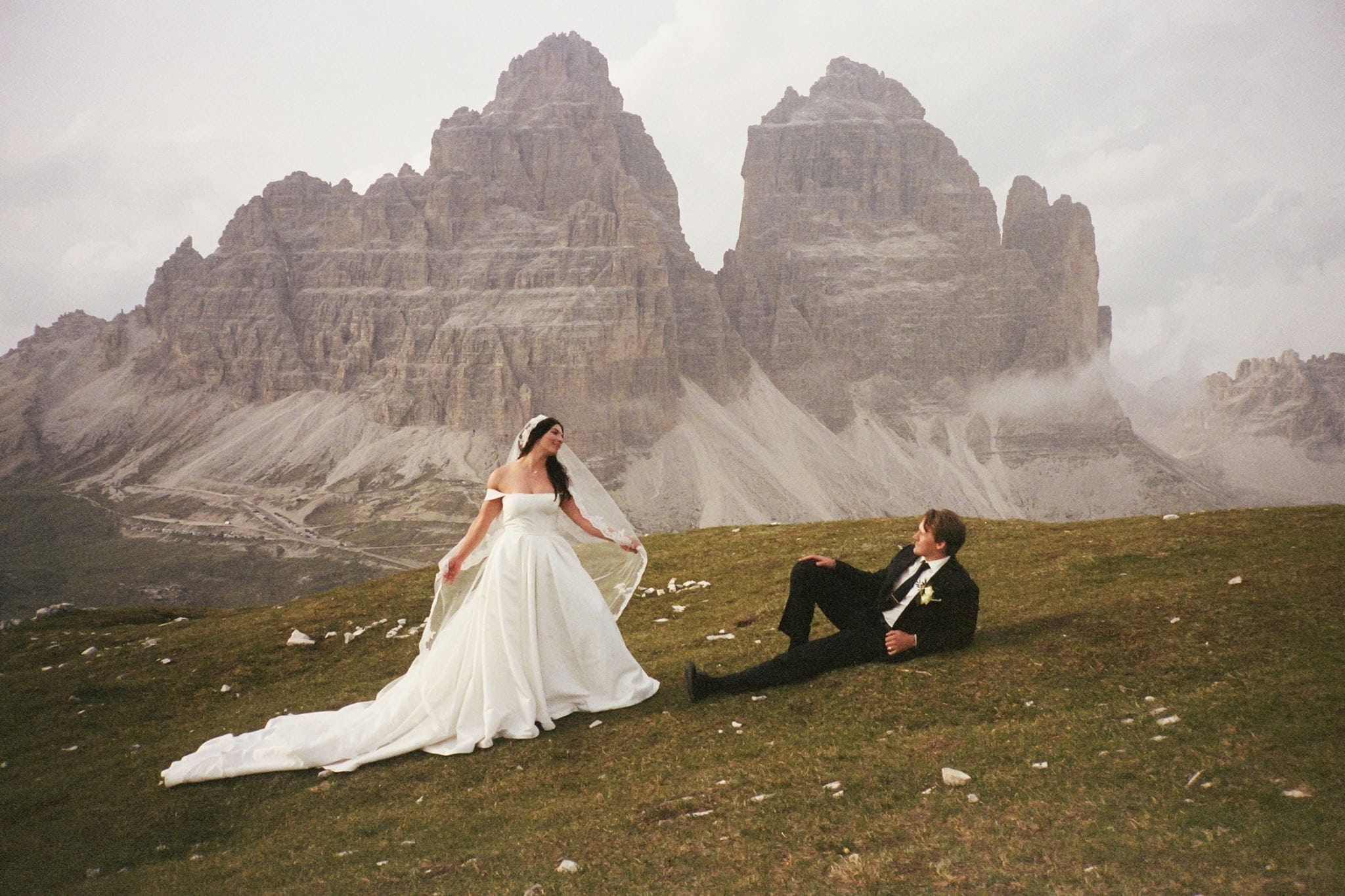 Groom lays on the ground and looks up at bride during their wedding in the Dolomite mountains.