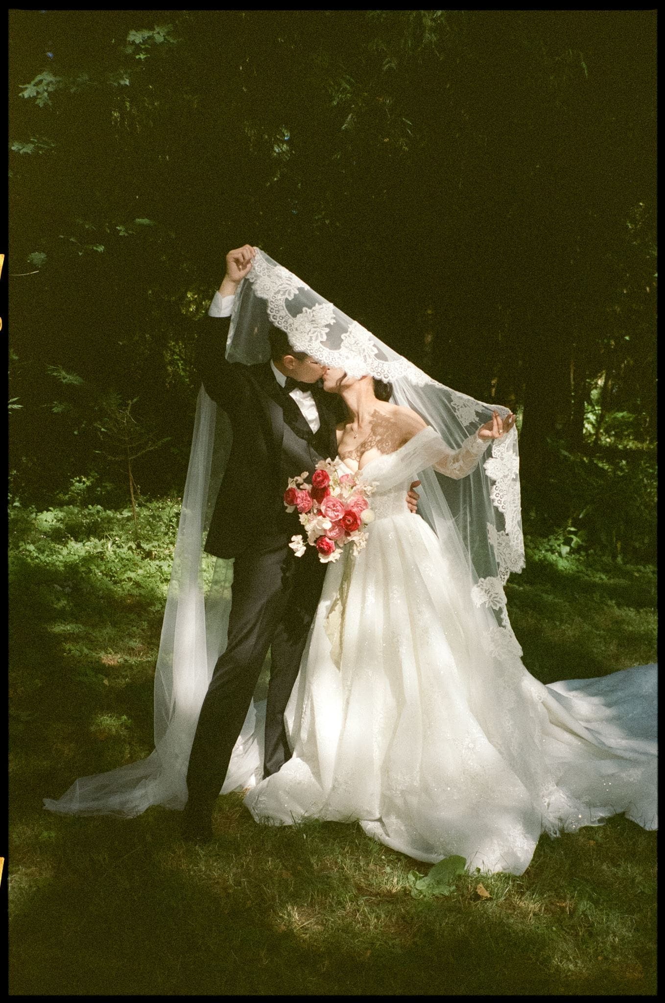 Newlyweds kiss under a lace veil during their film photography wedding session.