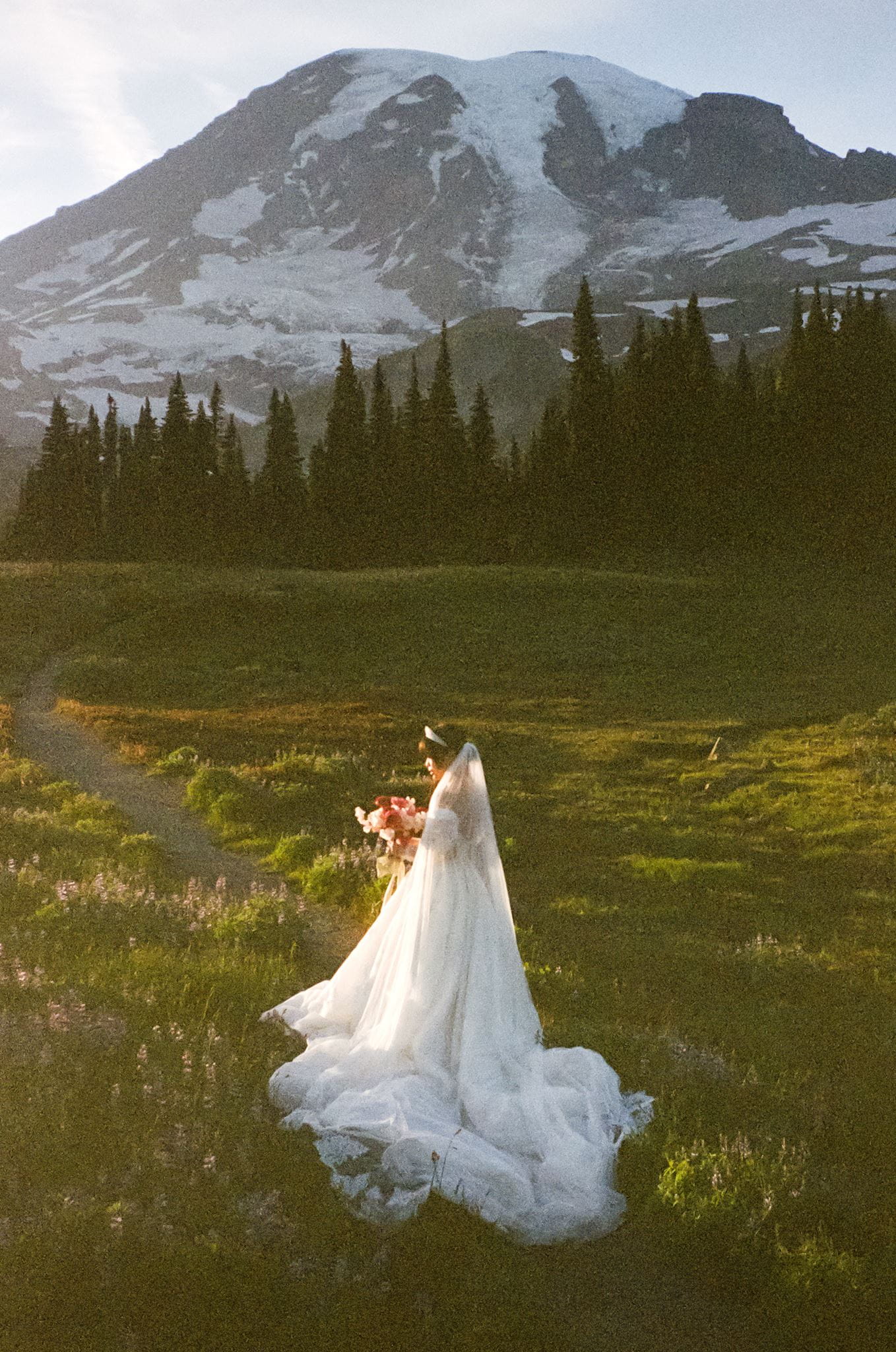 Bride stands on a mountain trail in her wedding dress during her bridal film portraits.