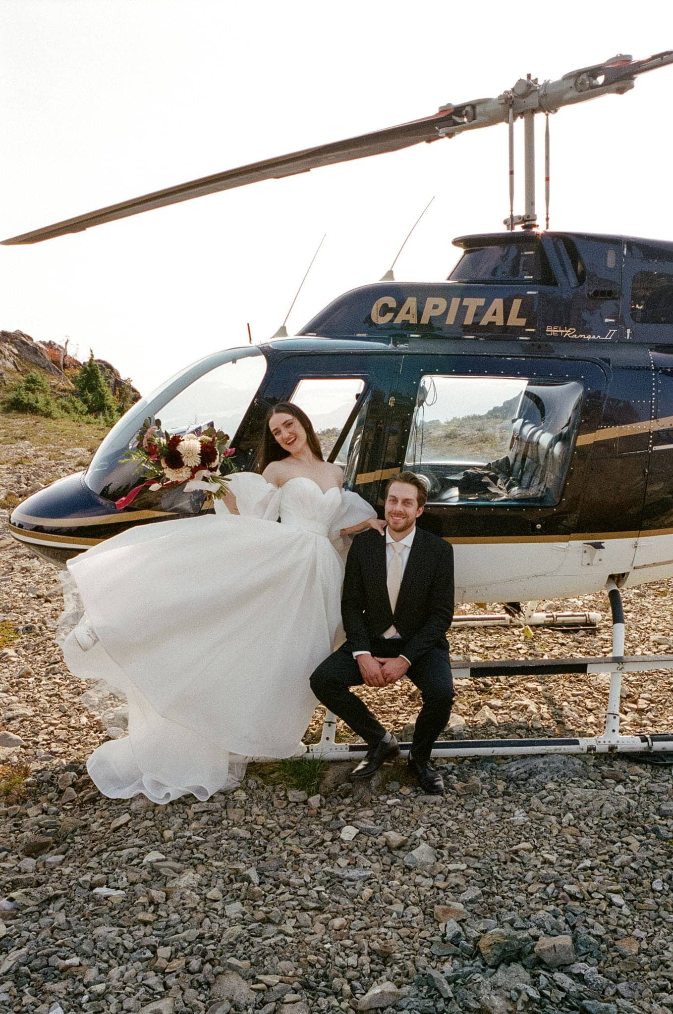 Bride and groom lean against a helicopter during their film wedding photo session in Tofino, BC, Canada.