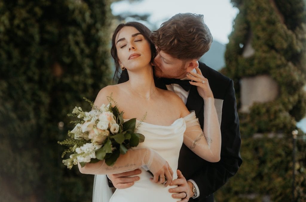 Groom kisses bride's neck during wedding portraits at their Lake Como wedding.