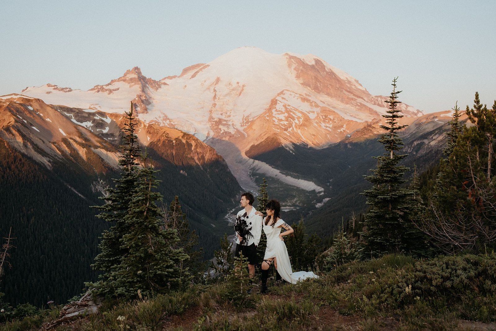 Newlyweds stand on a mountain trail in front of Mt Rainier during their sunrise adventure elopement in Washington.