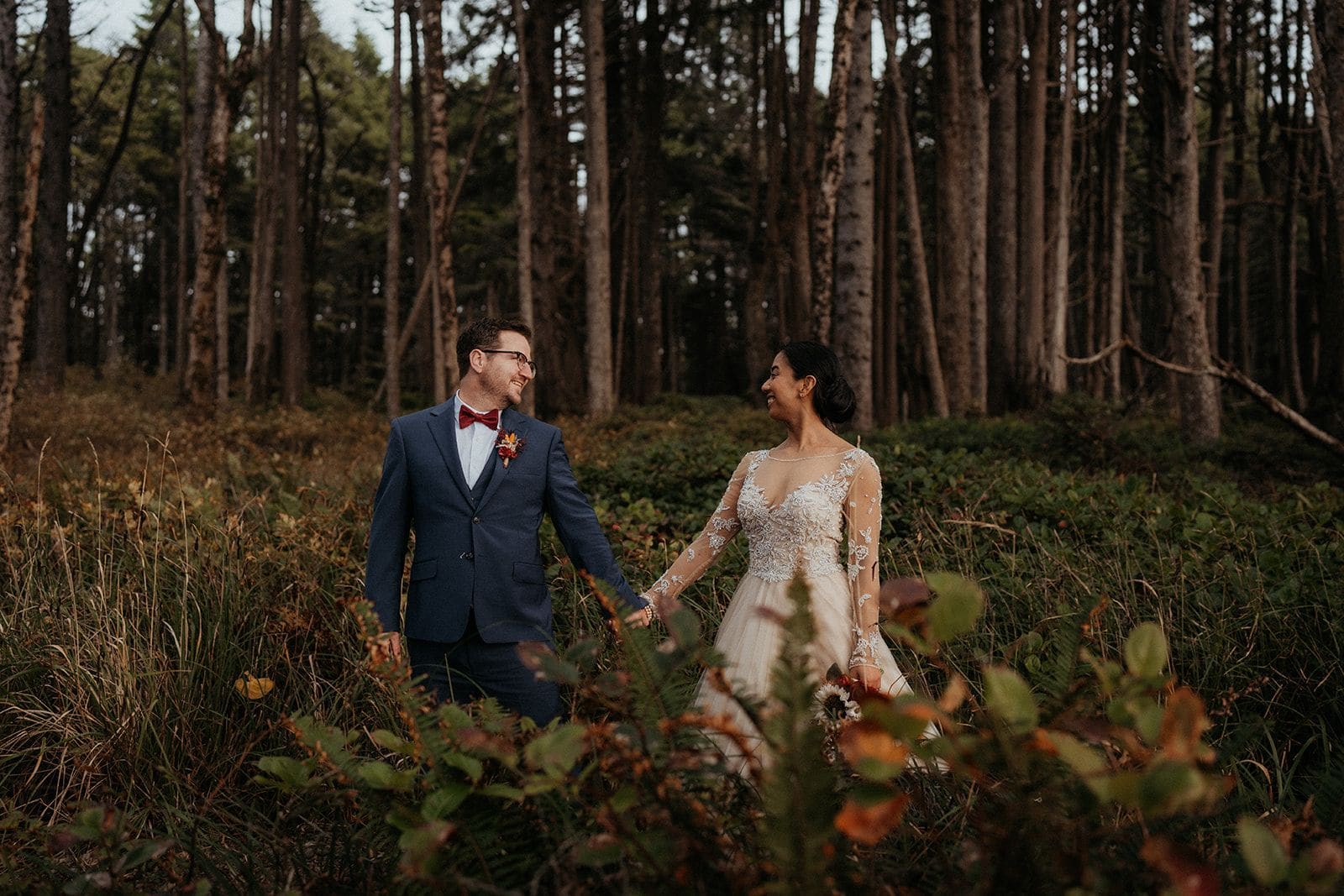 Bride and groom hold hands walking through the forest on the Olympic Peninsula.