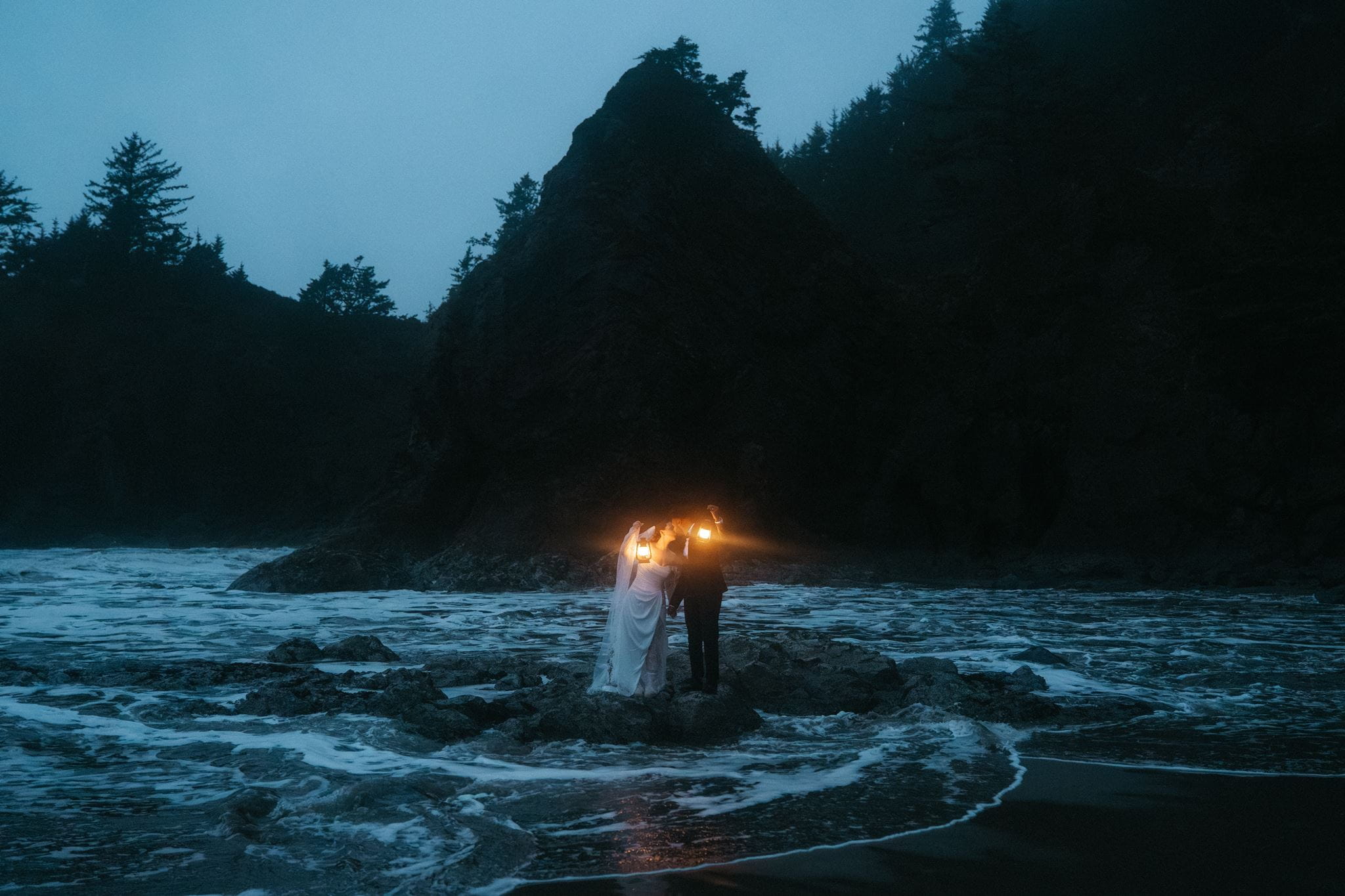 Newlyweds kiss while holding lanterns on the Pacific Coast during their two day wedding.