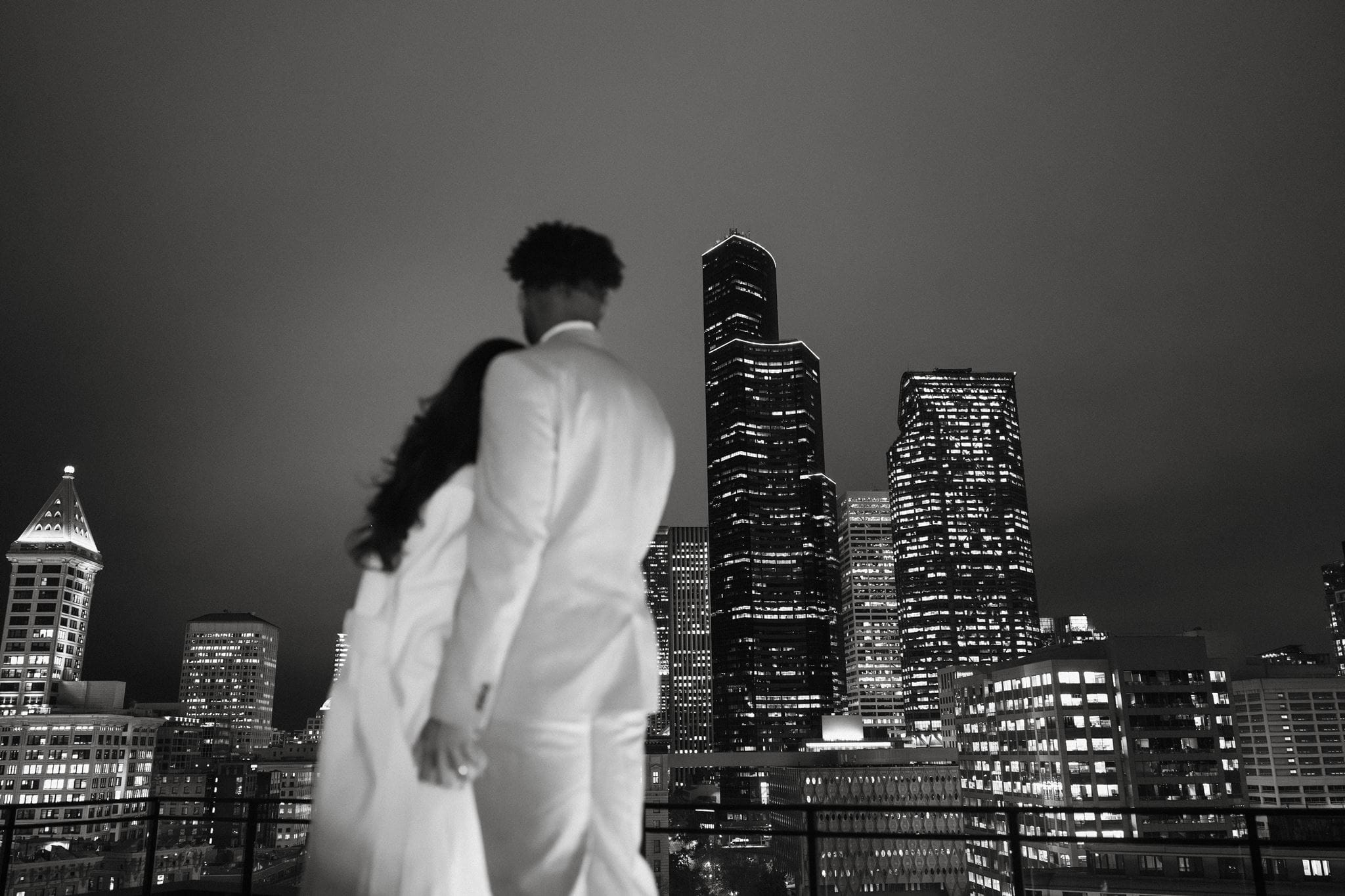 Newlyweds embrace on a rooftop while looking out at the Seattle city skyline after their courthouse wedding.