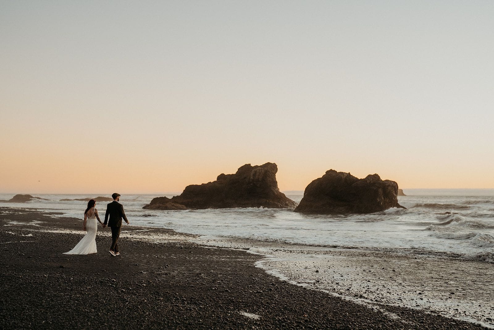 Newlyweds hold hands and walk on the beach during sunset on the Olympic Coast.