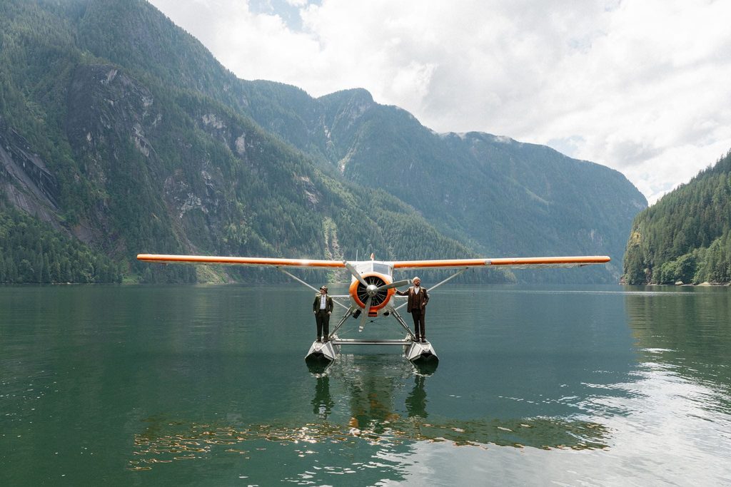 Grooms stand on a seaplane in the water during their PNW elopement on the Sunshine Coast, Canada.